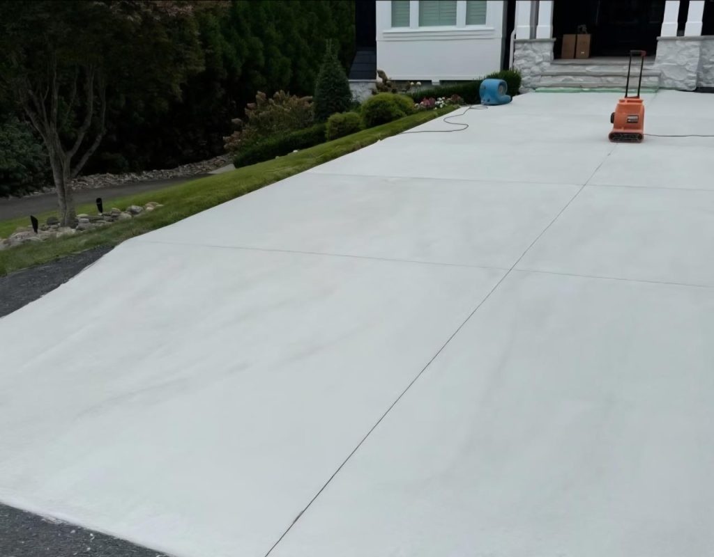 Freshly poured concrete driveway in front of a house, with tools and hose on the surface.