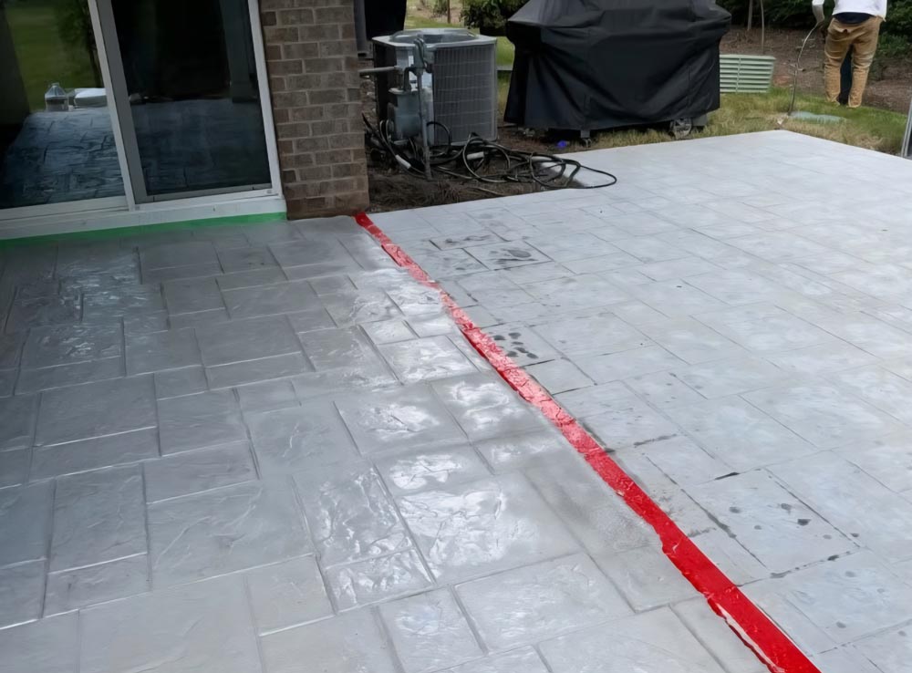 Freshly sealed patio with wet cement look, divided by a red tape line; person standing in background.