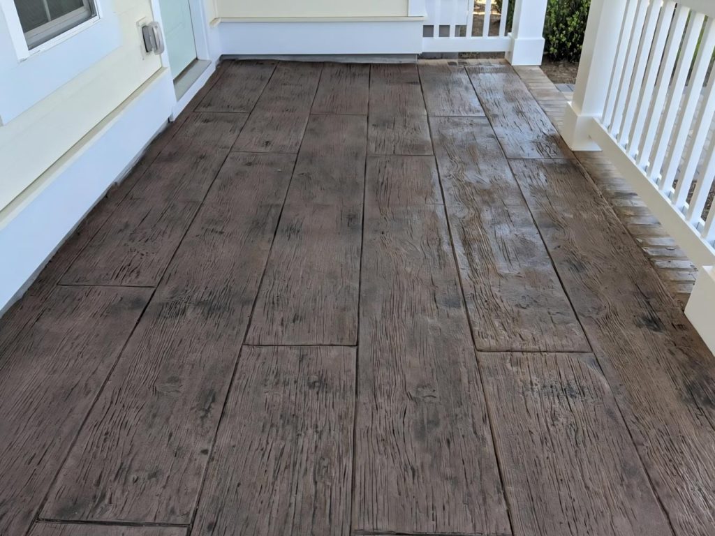 A porch with flooring designed to look like wood planks, bordered by white railings and walls.
