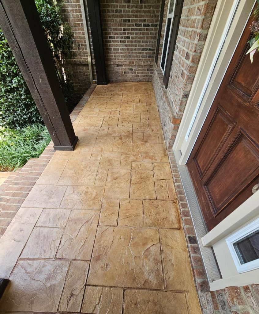 Front porch with stamped concrete flooring, brick walls, and a wooden door.