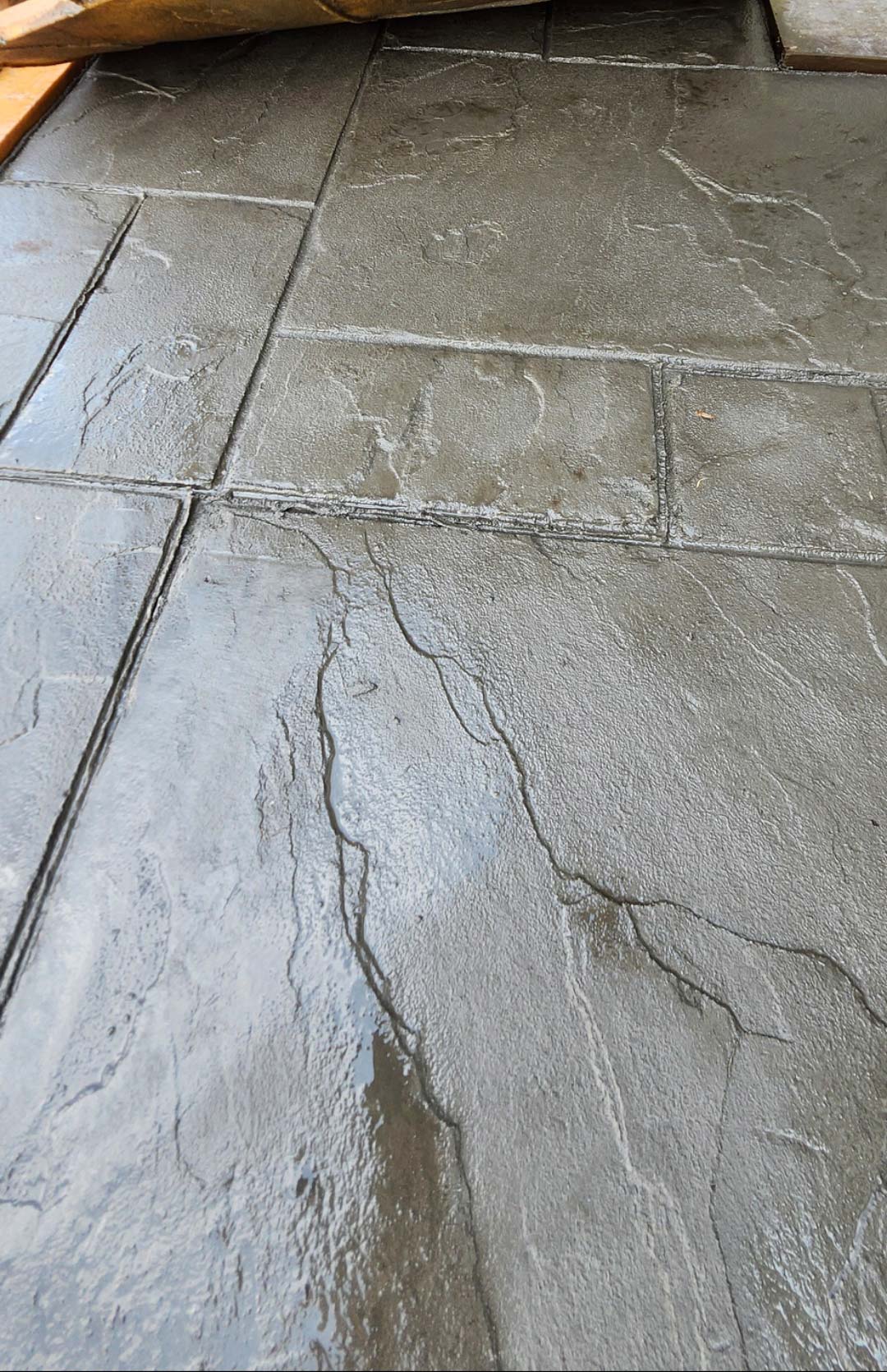 Stamped-1 Wet, dark gray stamped concrete tiles with a natural stone pattern and visible grout lines.