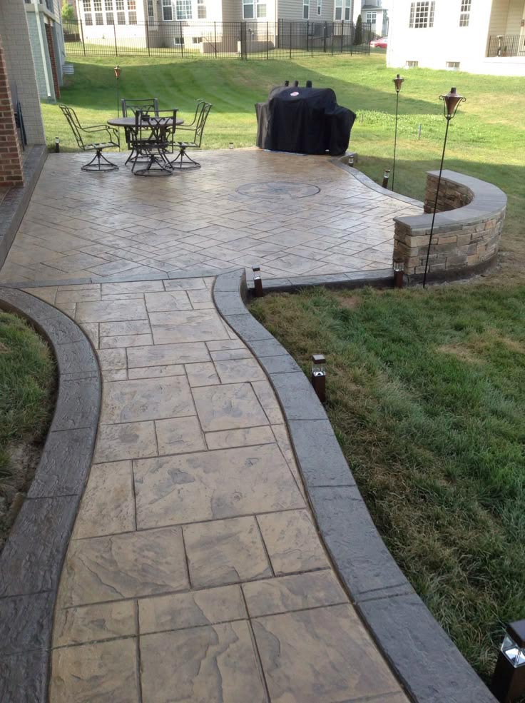 Stamped concrete patio with a curved walkway, outdoor dining set, grill, and lawn area.