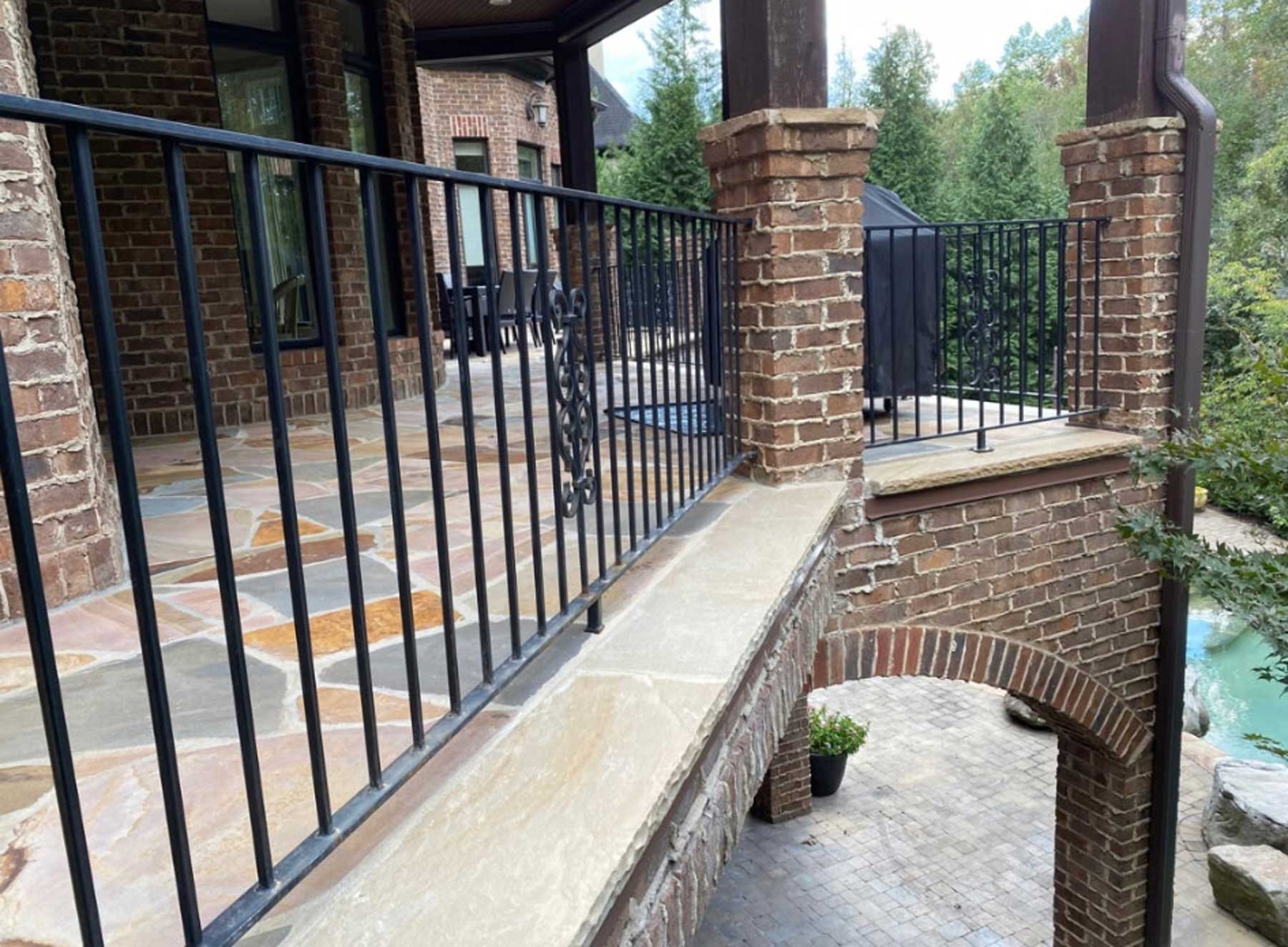 Brick patio with black metal railings, stone floor, and a stone archway leading to a lower courtyard.