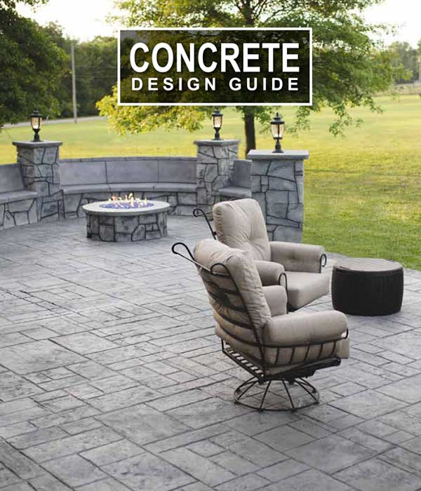 Outdoor patio with stamped concrete, cushioned chairs, fire pit, and stone wall, under trees by open grass.