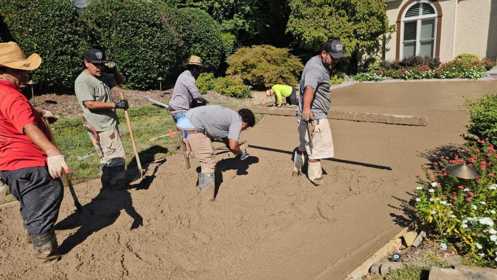 A crew of five workers smoothing wet concrete to form a new driveway.