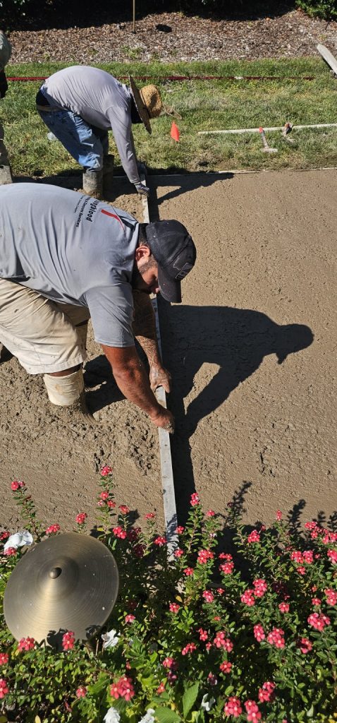 Two construction workers use a metal screed to level fresh concrete.