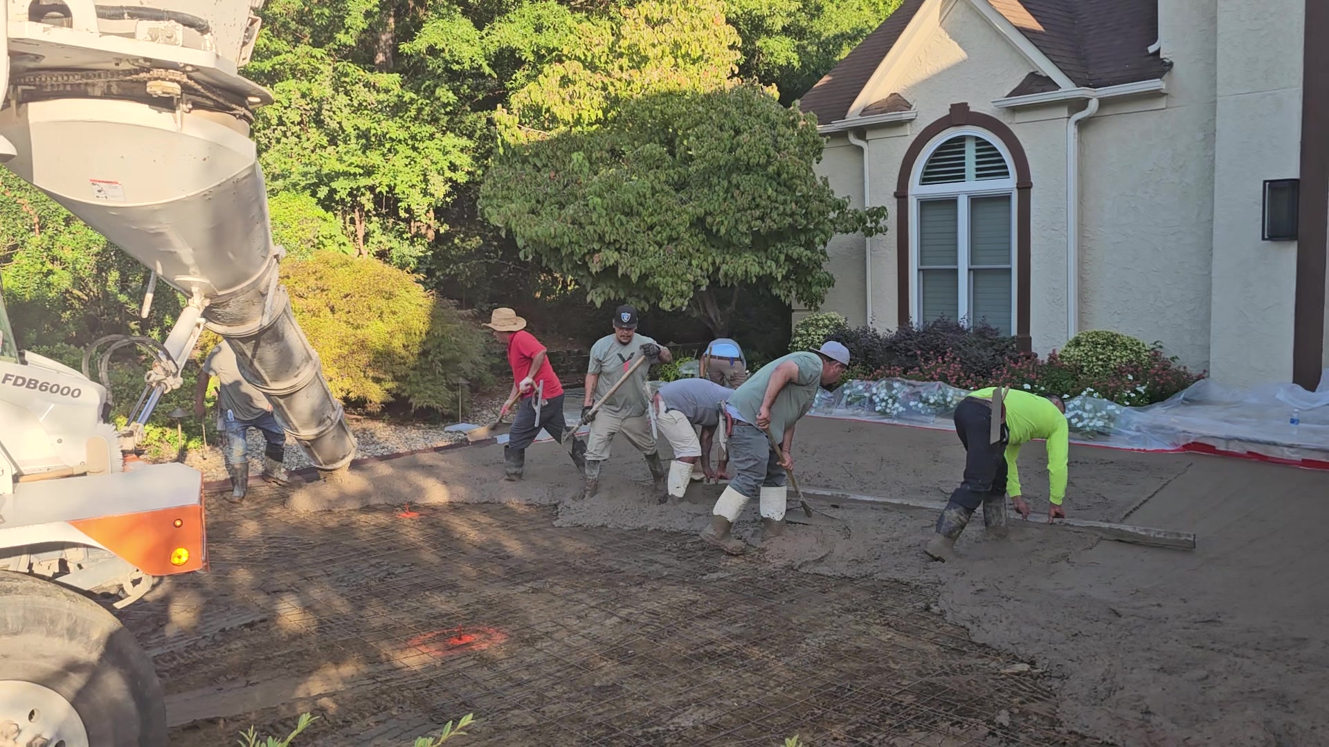 What a Finished Driveway Should Actually Look Like (Before You Sign a Contract) Construction workers using tools to smooth wet concrete poured from a truck.